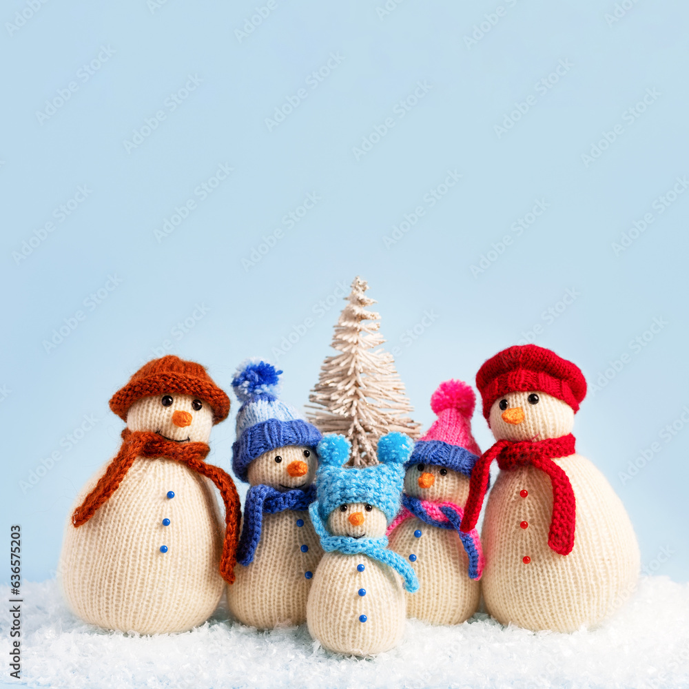 Fototapeta premium Knitted snowmen in colorful hats and scarves on a blue background. Concept of Christmas, New Year and winter fairy tale. Creative knitting of toys for children, home decoration.