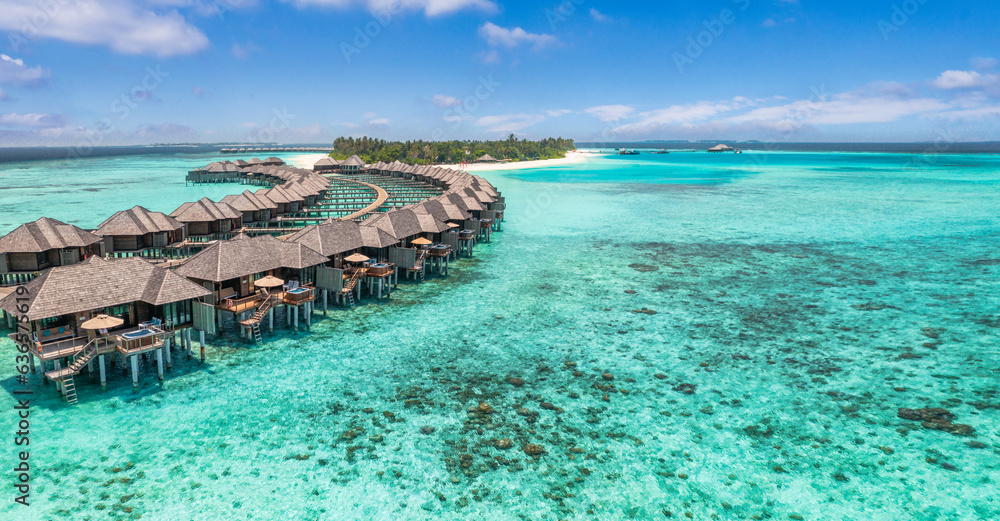 Aerial view of Maldives island, luxury water villas wooden pier path resort. Beautiful sky and ocean bay beach background. Summer vacation travel destination. Paradise aerial landscape panoramic coast