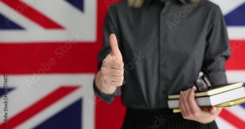 Woman with textbook and notebook makes thumb up after studying English. British flag wall shows respect for English language learning slow motion photo