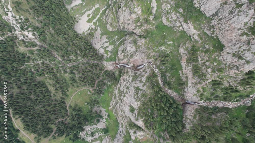 A high waterfall cascades in a mountain gorge. Coniferous trees, Christmas trees and grass grow. The river runs. Hiking trails. Top view from a drone. Sunset. Burkhan Bulak Waterfall, Kazakhstan A high waterfall cascades in a mountain gorge. Coniferous trees, Christmas trees and grass grow. The river runs. Hiking trails. Top view from a drone. Sunset. Burkhan Bulak Waterfall, Kazakhstan