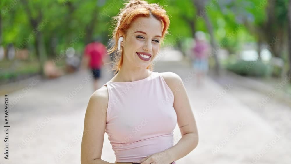 Young redhead woman wearing sportswear and earphones smiling at park Young redhead woman wearing sportswear and earphones smiling at park