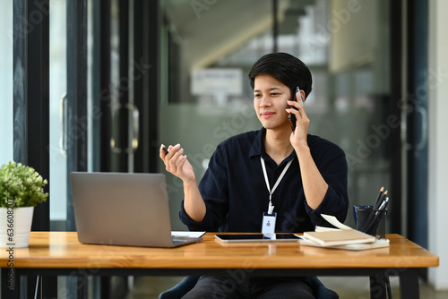 Handsome male financial advisor looking at laptop screen, talking on mobile phone with client