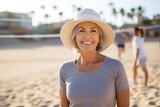 portrait of smiling senior woman in hat with friends playing volleyball on beach