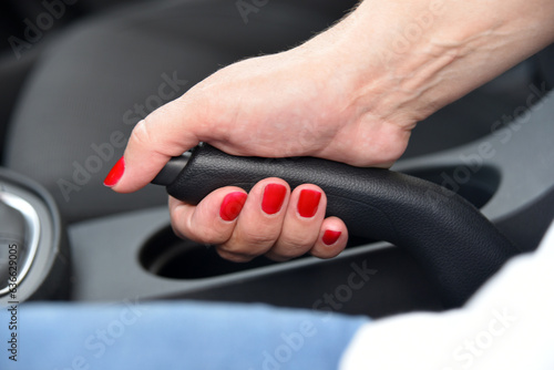 Hand female driver pulling the hand brake inside car