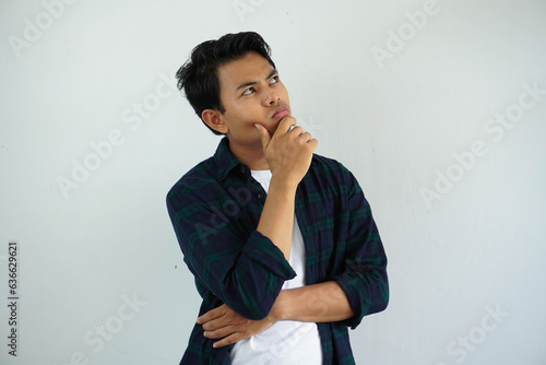 young asian man showing thinking pose with hand touching the chin while his eyes looking to the up isolated on white background.