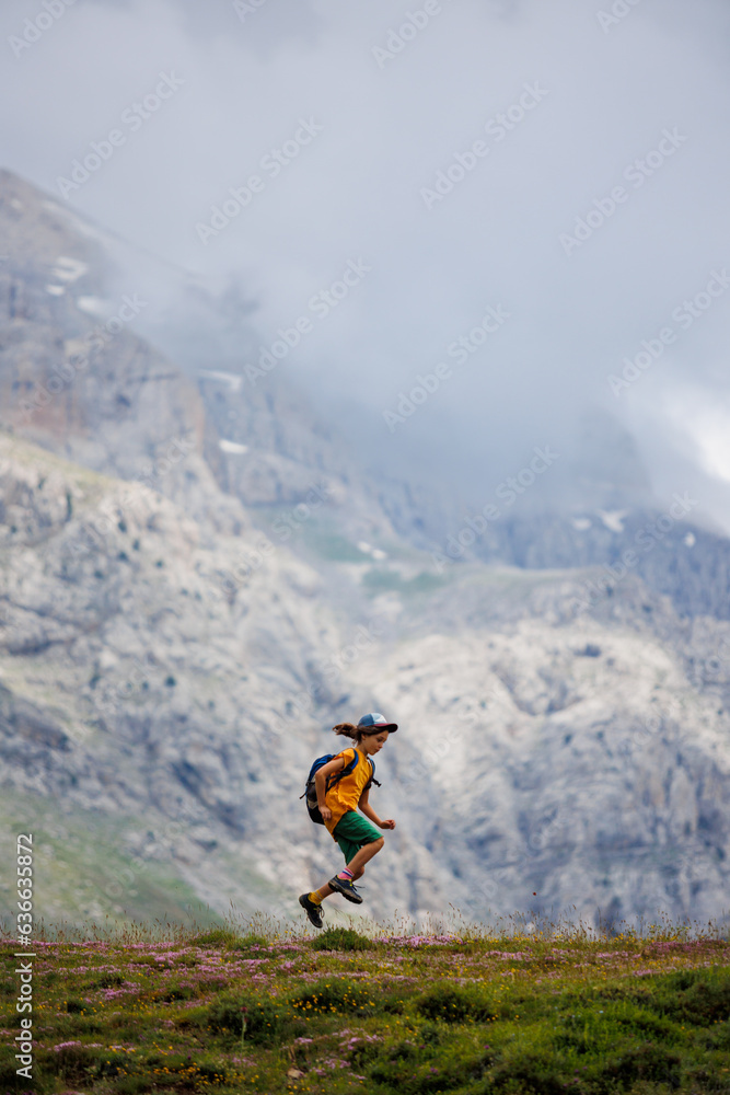 Obraz premium boy with a backpack on a hike against the backdrop of the mountains. child traveler with backpack, hiking, travel, mountains in the background, kids summer vacation.