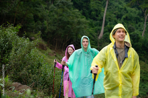 Group of friends in raincoats walking on the forest path, Hiking concept.