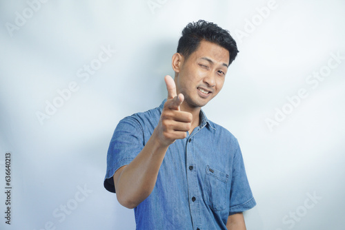 Young handsome Asian man wearing blue shirt over white background pointing to you and the camera with fingers, smiling positive and cheerful