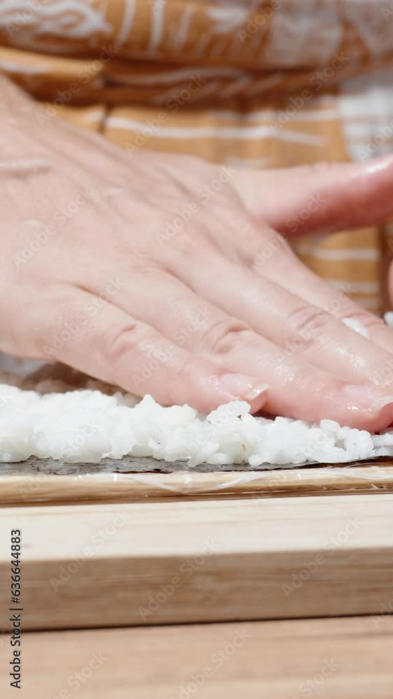 Vertical video. The woman spreads rice on the dry nori seaweed sheets using bamboo sticks. Vertical video. The woman spreads rice on the dry nori seaweed sheets using bamboo sticks.