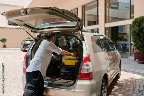 Man unloading car at hotel entrance, taking out suitcases