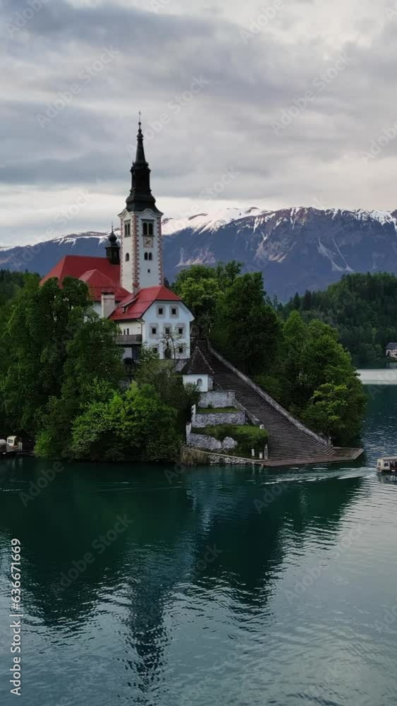 Aerial view of Bled lake and boat with the Pilgrimage Church of the Assumption of Maria on a small island after sunset, Slovenia. Vertical video Aerial view of Bled lake and boat with the Pilgrimage Church of the Assumption of Maria on a small island after sunset, Slovenia. Vertical video