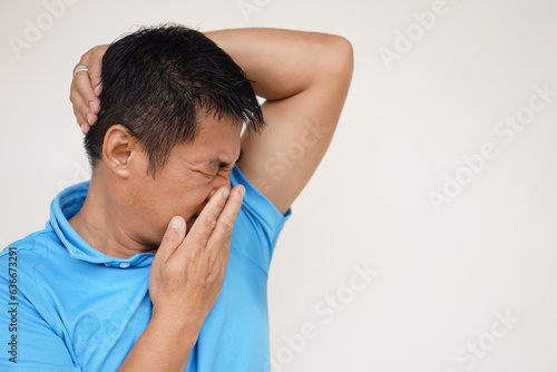 Asian man is checking his odor underarm, close his nose with hand, feel disgusted the body strong smell. Concept , health problem. Unpleasant body odor , smell nasty reaction. Negative emotion.        photo