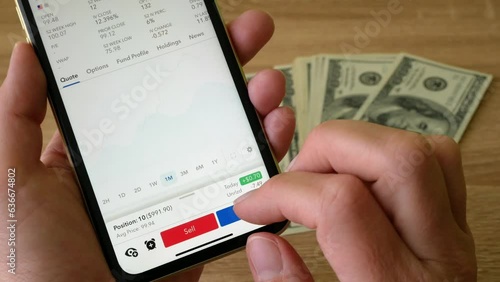 Wallpaper Mural Hand holding mobile phone with broker's app for buy and sell stock shares, bonds  exchange-traded fund (ETF), options, futures and money cash on table background, online trading concept Torontodigital.ca