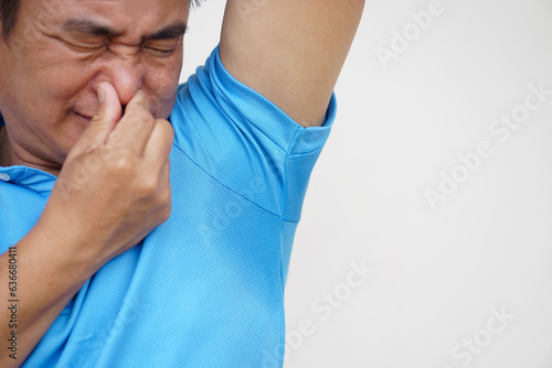 Asian man is checking his odor underarm, close his nose with hand, feel disgusted the body strong smell. Concept , health problem. Unpleasant body odor , smell nasty reaction. Negative emotion. 