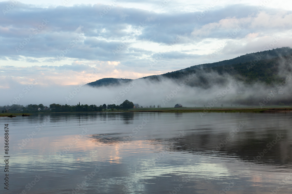 Dramatic misty sunrise sky with clouds in pink and blue tones over the Gouffre River, Baie-Saint-Paul, Charlevoix, Quebec, Canada
