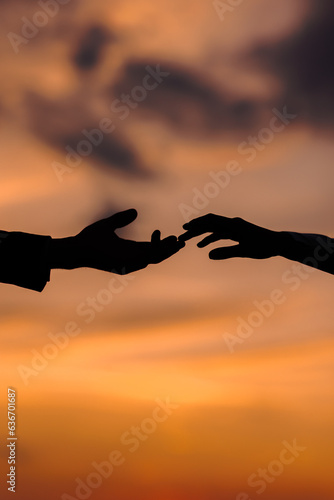 Valentine day. Silhouette of hands of woman and man reaching each other, touching fingers with tenderness on orange sunset sky background. Helping hands, save and support people concept. Friendship
