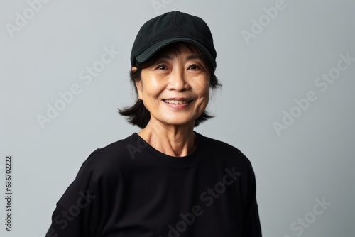 Medium shot portrait of a Chinese woman in her 60s in a white background wearing a cool cap or hat