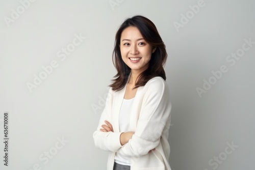 Portrait of a beautiful young asian businesswoman standing with arms crossed over gray background