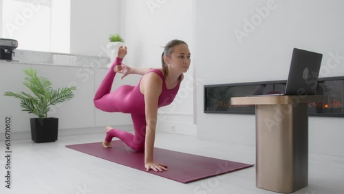 Young sporty woman in pink sportswear exercising at home using laptop. Fitness coach or pilates trainer teaching online class exercise or yoga course