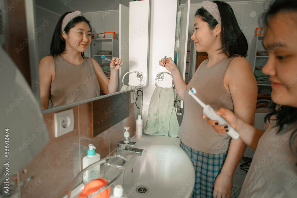 two asian girls sitting on the edge of a bathtub, applying toothpaste to their toothbrushes and laughing cheerfully two asian girls sitting on the edge of a bathtub, applying toothpaste to their toothbrushes and laughing cheerfully