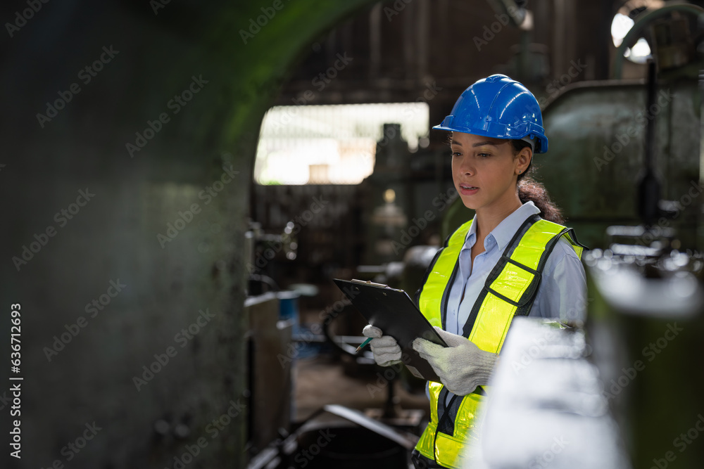 Female engineer in vest and helmet safety with clipboard checking and repairing machine at heavy metal factory. Preventive Maintenance concept Female engineer in vest and helmet safety with clipboard checking and repairing machine at heavy metal factory. Preventive Maintenance concept