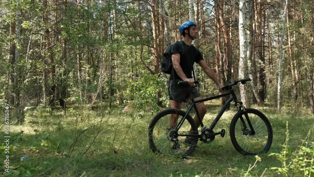 mountain bike.An active lifestyle.A cyclist wearing a helmet and carrying a backpack walks with a mountain bike through the forest and looks around .Slow motion mountain bike.An active lifestyle.A cyclist wearing a helmet and carrying a backpack walks with a mountain bike through the forest and looks around .Slow motion