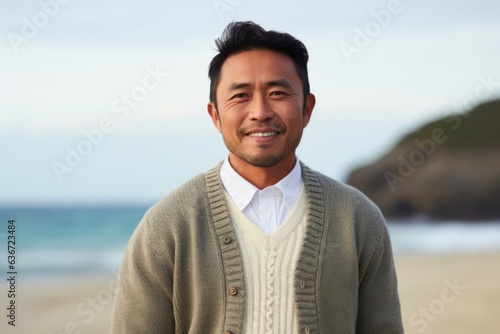 Medium shot portrait of a Indonesian man in his 40s in a beach background wearing a chic cardigan