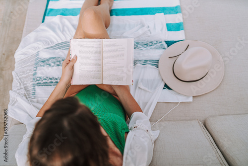 Chica joven en traje de baño leyendo libro en cama balinesa en piscina de hotel de lujo