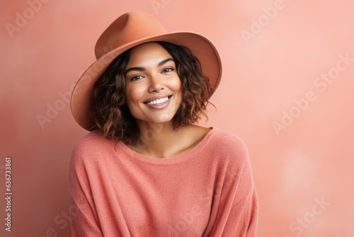 Portrait of a beautiful young woman wearing hat and sweater on a pink background