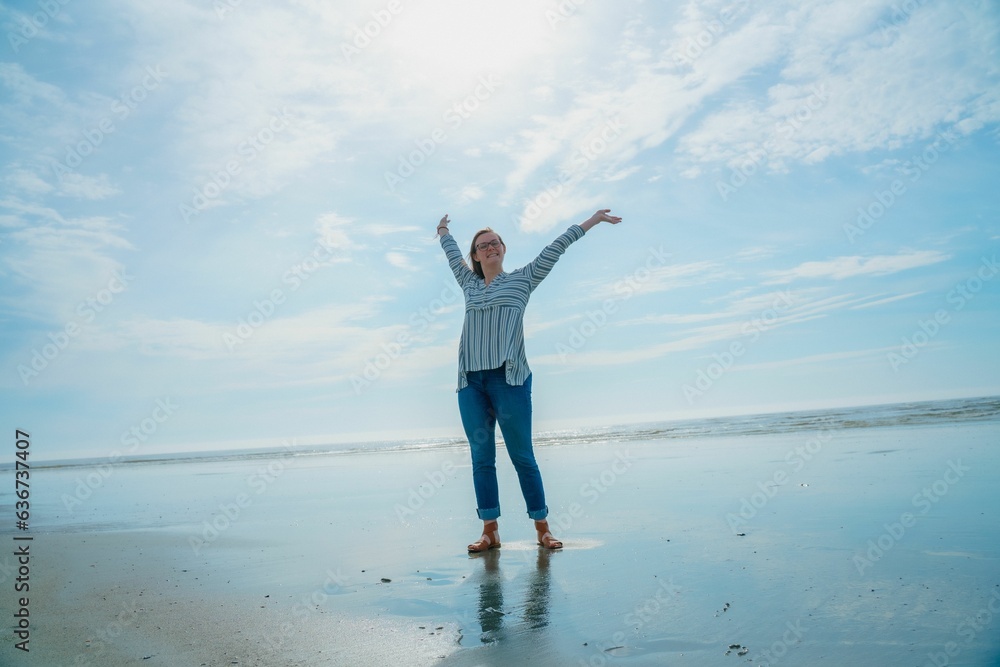 woman with arms outstretched on beach standing near water with sky in background woman with arms outstretched on beach standing near water with sky in background