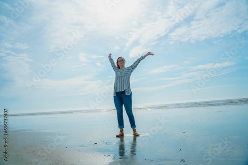 woman with arms outstretched on beach standing near water with sky in background
