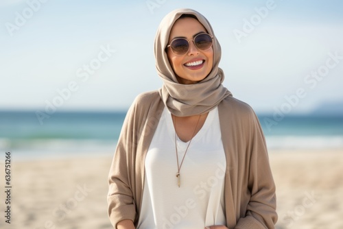 Portrait of a smiling young woman wearing sunglasses and hijab on the beach