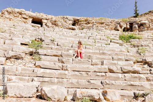 Tourists take pictures of the ruins of the old city. A young beautiful woman sits on stone seats in an ancient amphitheater.