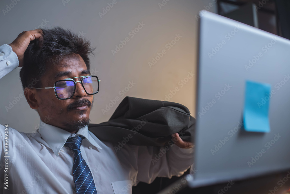 businessman sits at his desk wearing a shirt and glasses, works through his laptop, and is visibly upset on the table in frustration. businessman sits at his desk wearing a shirt and glasses, works through his laptop, and is visibly upset on the table in frustration.