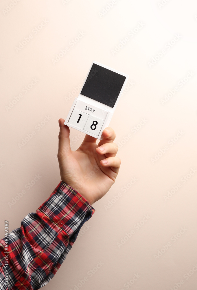 Date May 18, block calendar in male hand on beige background Date May 18, block calendar in male hand on beige background