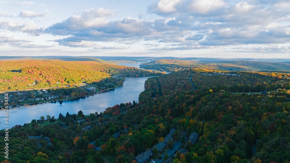 Aerial of a scenic lake surrounded by a dense forest with autumn foliage in fall colors
