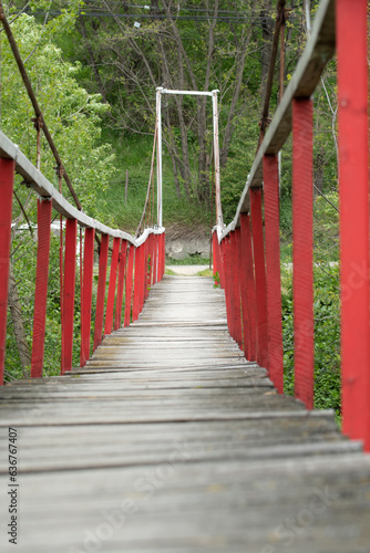 A wooden red footbridge with railings crossing a river.