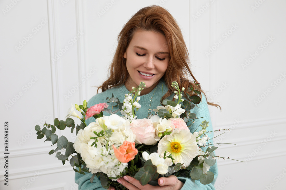 Beautiful woman with bouquet of flowers near white wall indoors Beautiful woman with bouquet of flowers near white wall indoors