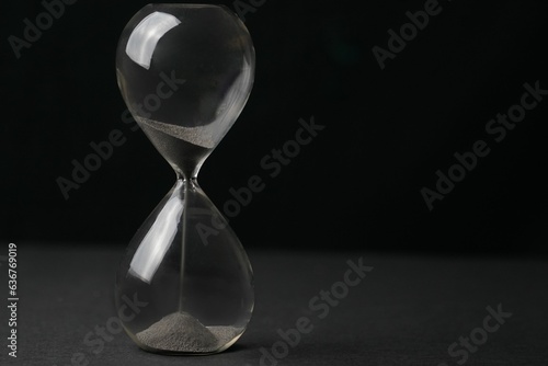 Hourglass with sand falling through, set against a black backdrop, the concept of time passing