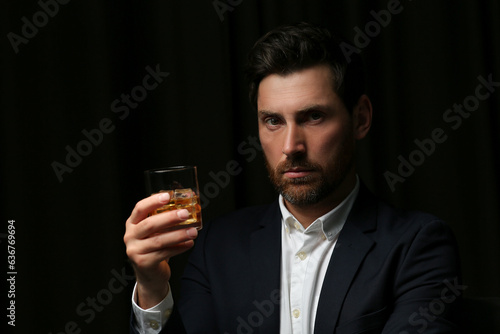Handsome man in suit holding glass of whiskey on black background © New Africa