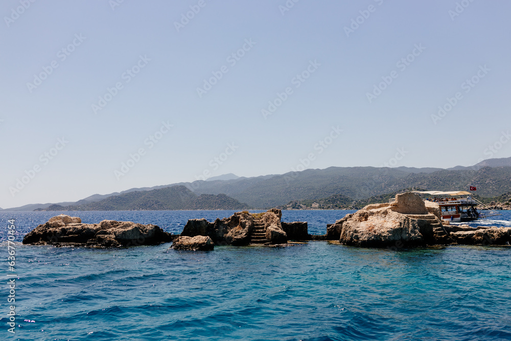Fototapeta premium Beautiful view of the Mediterranean Sea with yachts. Picturesque landscape of blue ocean and green mountains on a sunny summer day. The sunken city of Kekova, Türkiye - 28 July 2023