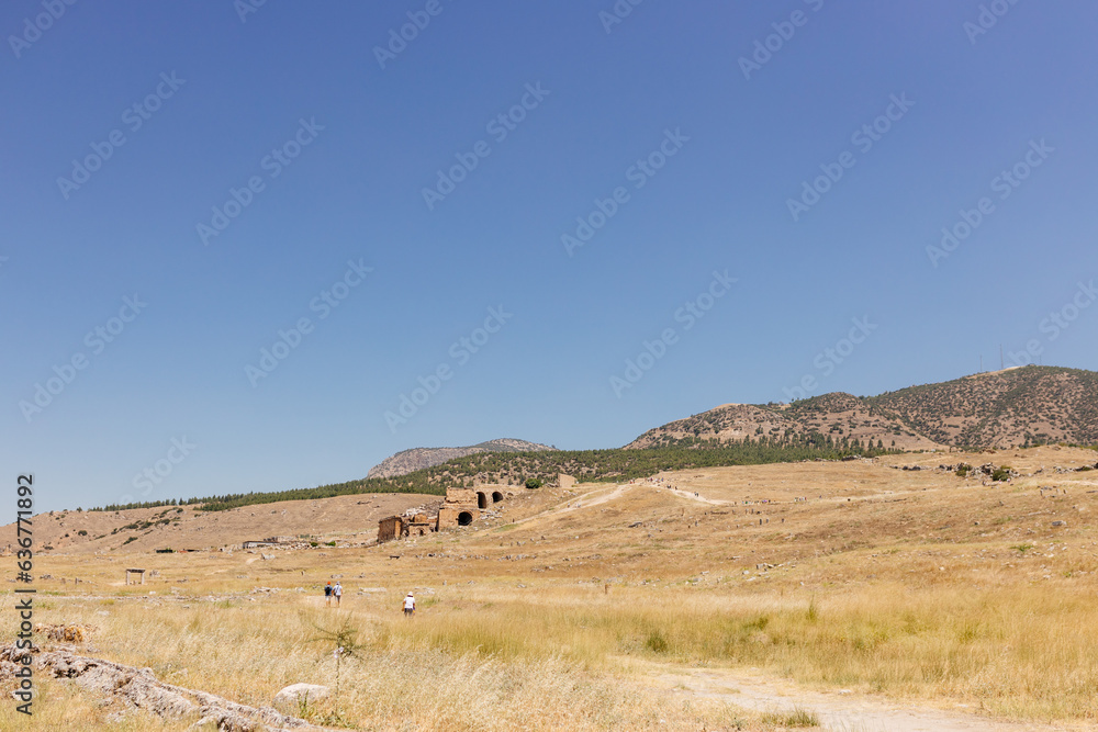 Half-ruined buildings of the ancient city, Journey to the old city. Preserved old columns against the backdrop of a mountain landscape. Hierapolis Ancient City, Pamukkale, Türkiye - July 29, 2023
