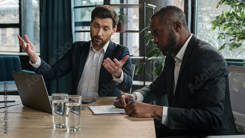 Caucasian manager showing African boss bad business result computer mistake two diverse men multiracial coworkers businessmen with papers and laptop sad upset failure discuss startup problem at office