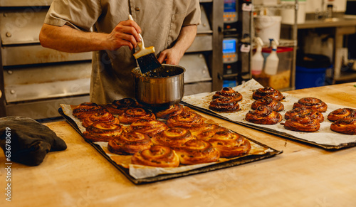 Baker brushes glaze onto freshly baked golden pastries in professional kitchen