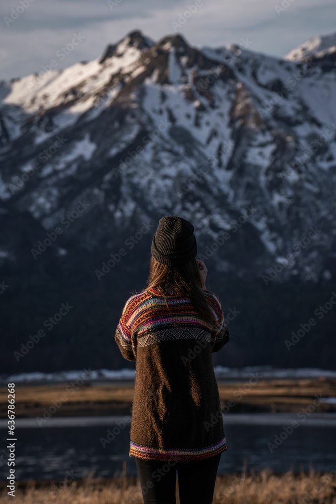 Vertical shot of a young woman standing on the background of the snowy mountain in the highland Vertical shot of a young woman standing on the background of the snowy mountain in the highland
