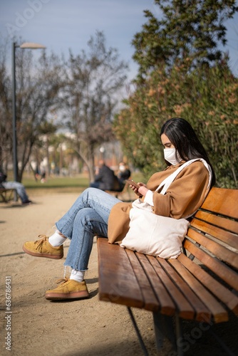 Young woman with a disability sitting on a park bench using a digital tablet for work