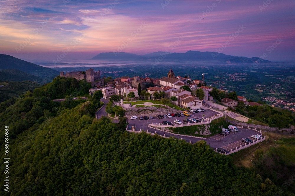 Aerial of a small Italian village set on top of a mountain with the pink glow of the sunrise.