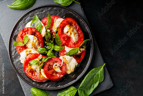 Italian caprese salad with mozzarella, tomatoes and basil on slate board. Plate of healthy classic delicious caprese salad on black plate