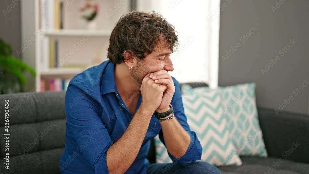 Young hispanic man sitting on sofa with serious expression at home Young hispanic man sitting on sofa with serious expression at home