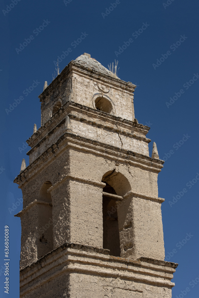 Torre de iglesia católica de adobe, antigua y rústica en un día soleado y con cielo azul